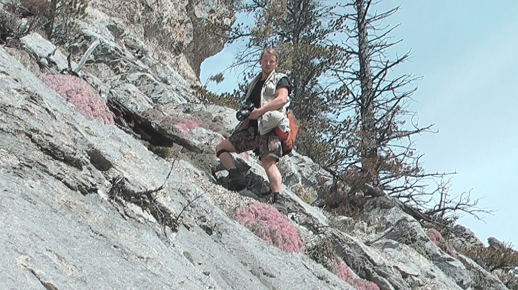 Jess Varnado balancing on the side of a steep rocky hillside, camera in hand